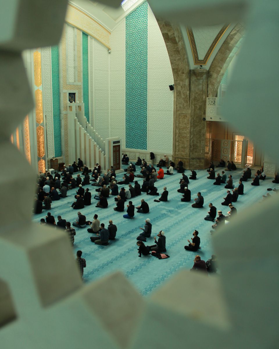 A congregation gathered inside a mosque, seen from the balcony