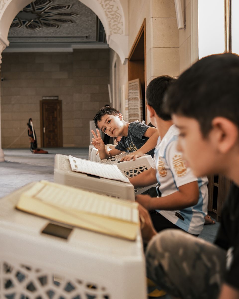Children studying the Quran at reading stands inside a mosque